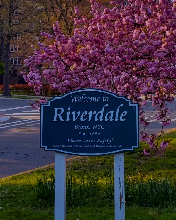 A Welcome to Riverdale sign under a tree in blossom at dusk