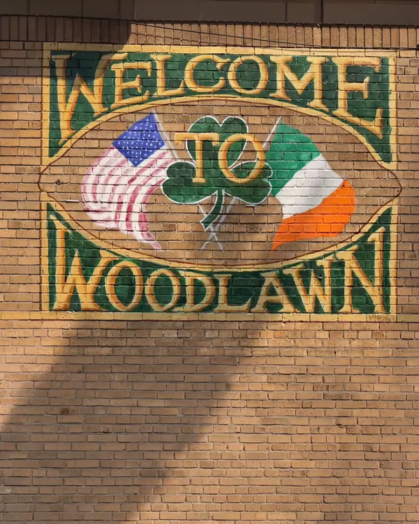 A painted Welcome to Woodlawn mural with a shamrock and American and Irish flags on a tan brick wall